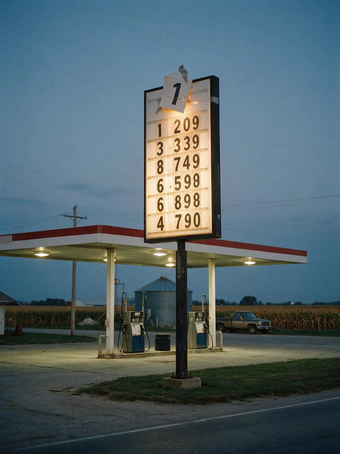 A rural gas station price sign that has run out of digit slots, with an extra numeral taped above the panel.